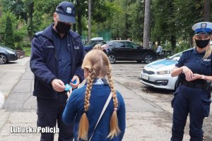 Policjanci wręczają dziewczynce elementy odblaskowe.