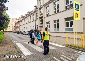 Policjantka stojąca przy przejściu dla pieszych, po którym przechodzą uczniowie idący do szkoły.