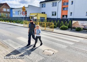 Policjantka przechodzi z dziewczynką przez przejście dla pieszych.