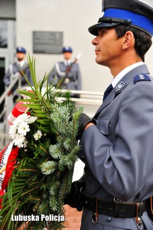 Policjant z posterunku honorowego z wieńcem. W tle policjanci