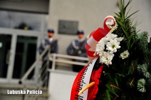 Wieniec kwiatów. W tle policjanci z posterunku honorowego