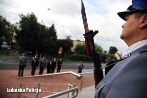 Policjant z posterunku honorowego. W tle uczestnicy uroczystości