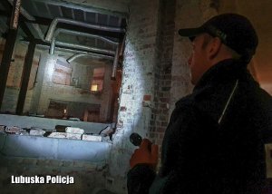 Policjant świecący latarką we wnętrzu opuszczonego budynku.