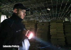 Policjant świecący latarką we wnętrzu opuszczonego budynku.