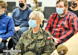 Kobieta w mundurze wojskowym siedzi obok innych osób na sali konferencyjnej.