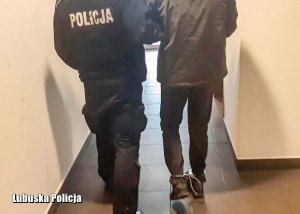 policjant prowadzi zatrzymanego wąskim korytarzem
