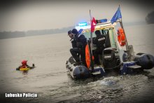 Policjanci na motorówce podczas ćwiczeń ratunkowych, obok motorówki mężczyzna przebywający w wodzie.
