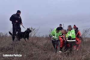 policyjny przewodnik z psem oraz ratownicy medyczni niosący mężczyznę do karetki