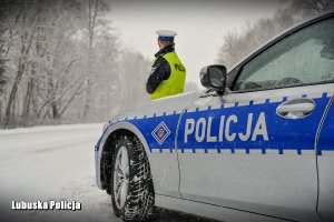 Policjant drogówki przy radiowozie policyjnym zimą.