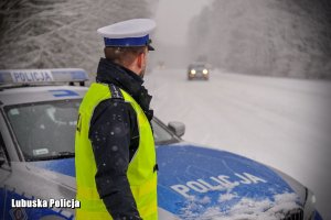 Policjant drogówki przy policyjnym radiowozie zimową porą.
