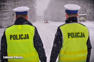 Policjanci drogówki stojący przy drodze zimową porą.