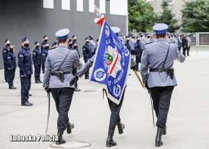 Sztandar Komendy Wojewódzkiej Policji w Gorzowie Wielkopolskim prowadzony przez policjantów na tle nowych kandydatów