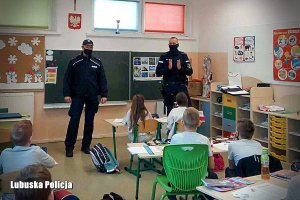 Dwóch policjantów przemawia do grupy dzieci w szkole