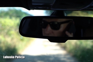 Lusterko wsteczne w samochodzie, na którym widać twarz mężczyzny w okularach.