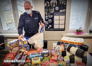 Policjant stojący pakuje artykuły spożywcze do torby.