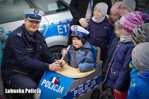 Policjant z dziećmi pozują do zdjęcia przy radiowozie policyjnym.
