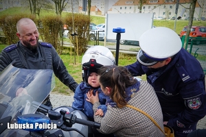 Mały chłopiec siedzący na policyjnym motocyklem w otoczeniu policjantów.