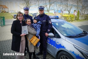 Mały chłopiec, jego mama i nauczycielka oraz policjanci pozujący do zdjęcia przy radiowozie policyjnym.