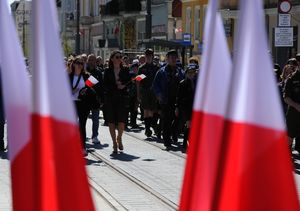 Przemarsz uczestników uroczystości na tle flag Polski