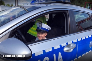 Chłopiec w radiowozie z czapką policjantka drogówki