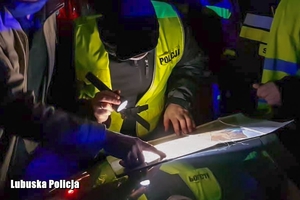 Policjanci w godzinach nocnych przy wykorzystaniu latarki przeglądają mapę