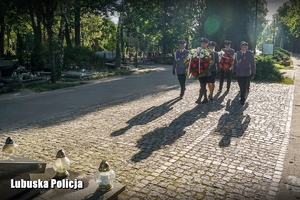 policjanci idą z kwiatami w kierunku Krzyża Katyńskiego