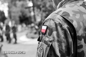 Czarno - białe zdjęcie, z biało czerwoną flagą Polski na ramieniu żołnierza.