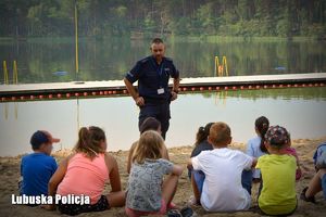Policjant podczas rozmowy profilaktycznej z dziećmi nad jeziorem.