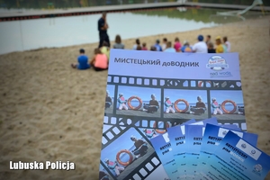 Ulotki profilaktyczne w języku ukraińskim, a w tle dzieci siedzące na plaży.
