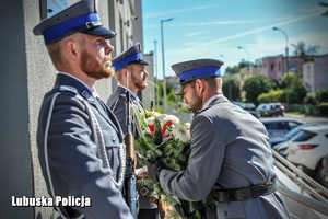 Policjant składa kwiaty przed pamiątkową tablicą.