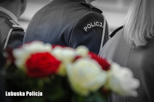 Zdjęcie policjantów, a na pierwszym planie wiązanka biało - czerwonych kwiatów