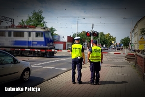 Policjant i funkcjonariusz ochrony kolei przed przejazdem kolejowym na którym przejeżdża pociąg