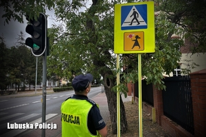 Policjant sprawdza stan techniczny znaków drogowych postawionych w rejonie szkół