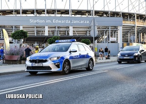 Policyjny radiowóz jadący jezdnią przy stadionie żużlowym.
