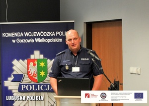 Policjant przemawiający z mównicy.