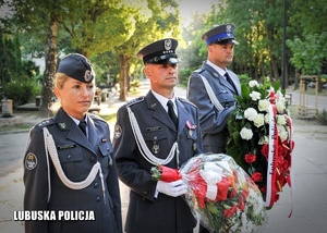 Funkcjonariusze służb mundurowych trzymający wiązanki kwiatów.