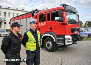 Strażak oraz policjant drogówki stojący przy pojeździe Straży Pożarnej.