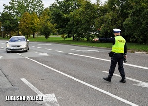 Policjant drogówki zatrzymuje pojazd osobowy do kontroli drogowej.