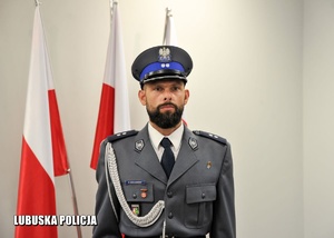 Policjant stojący na tle flag Polski.