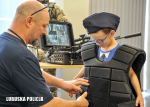 Policjant ubiera kamizelkę ochronną chłopcu.