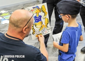 Policjant pokazuje chłopcu grafikę z policyjna maskotką.