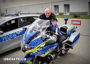 Chłopiec na motorze policyjnym pozuje wraz policjantem do zdjęcia.