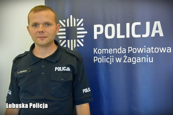Policjant przy logo komendy w Żaganiu