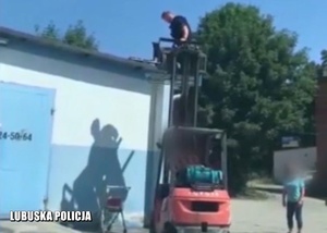 Policjant przy użyciu wózka widłowego próbuje ściągnąć psa z dachu.