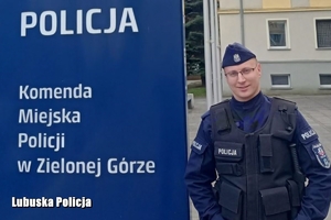 policjant stoi przy banerze Komendy Miejskiej Policji w Zielonej Górze