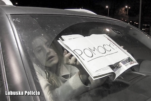 kobieta w samochodzie z kartką przy szybie z napisem POMOCY
