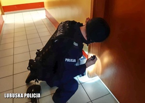 Policjant podczas oględzin walizki na korytarzu.