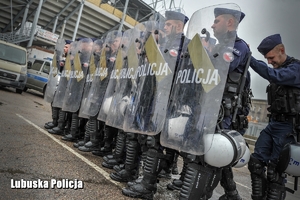 Policjanci oddziałów prewencji stojący w rzędzie z tarczami ochronnymi.