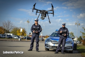 Policjanci na tle radiowozu sterują dronem