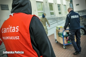 Wolontariusz Caritasu, a w tle policjanci przenoszą prezenty.